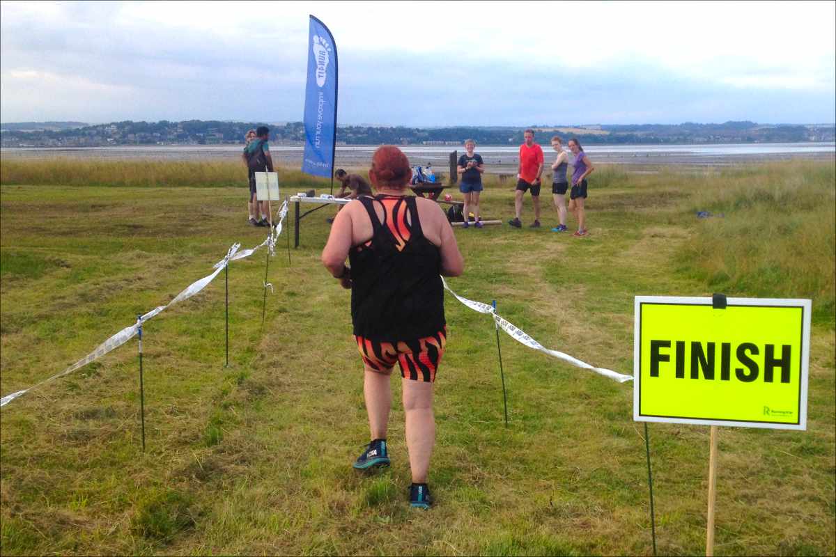 photo of a runner passing a sign saying finish, following the path between tapes..