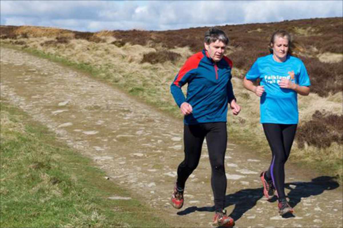 photo of two runners on a gravel road that is running along a hillside ridge.