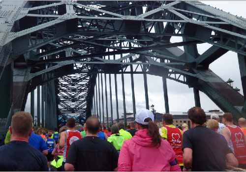 photo of runners passing under the iron superstructure of the Tyne Bridge in Newcastle.