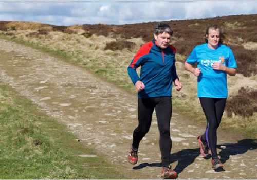 photo of two runners on a gravel road that is running along a hillside ridge.